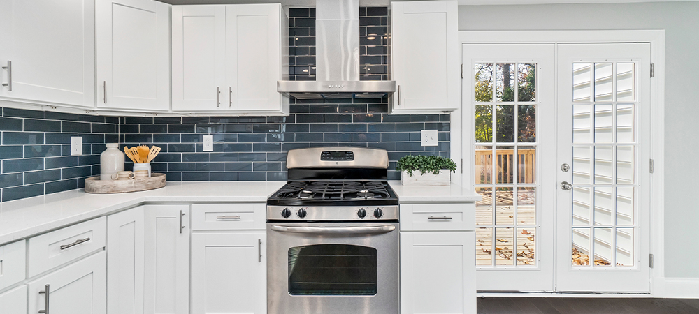 A modern kitchen with white cabinets, a blue glass tile backsplash, and stainless steel appliances