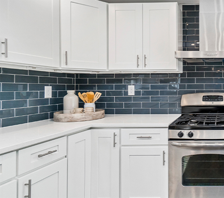 A modern kitchen with white cabinets, a blue glass tile backsplash, and stainless steel appliances