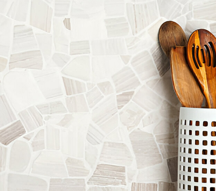 Textured white ceramic mosaic backsplash with irregular pattern shown with wooden utensils in decorative holder