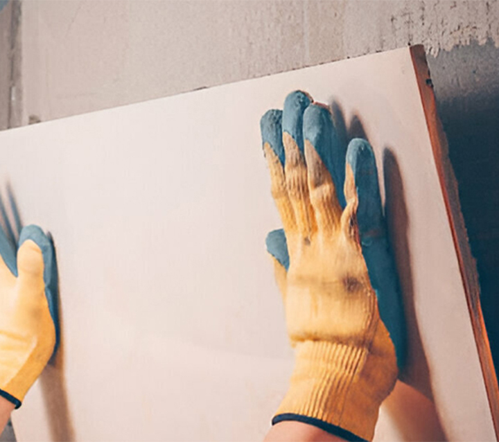 Close-up of gloved hands installing a large format tile backsplash