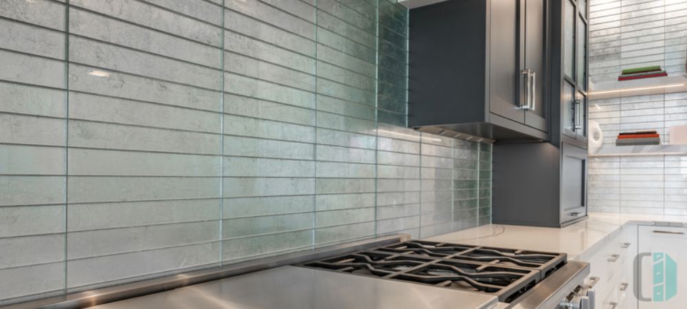 A modern kitchen with gray cabinets and a glass tile backsplash