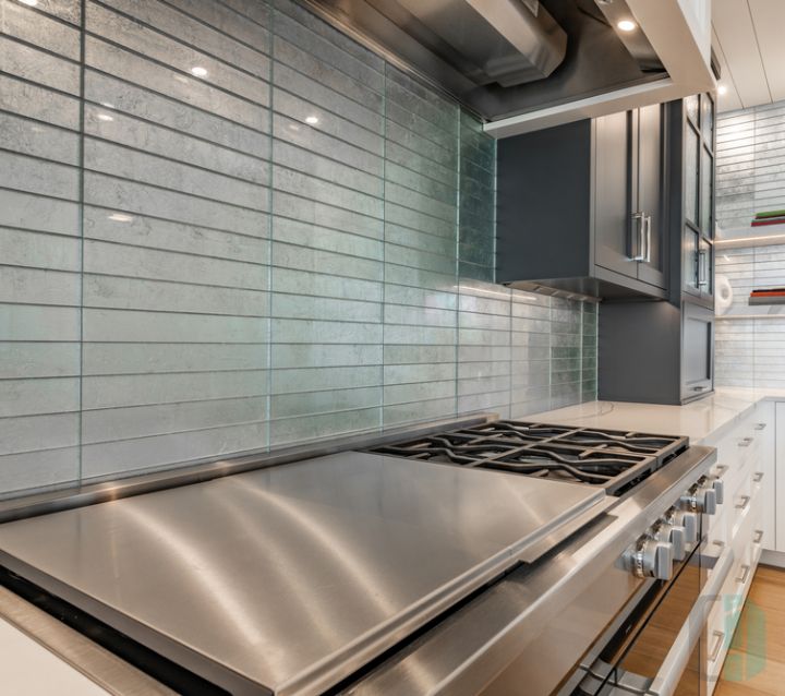 A modern kitchen with gray cabinets and a glass tile backsplash