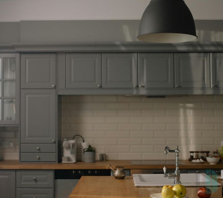 A kitchen with gray shaker cabinets and a natural stone backsplash featuring a mix of white and gray tones