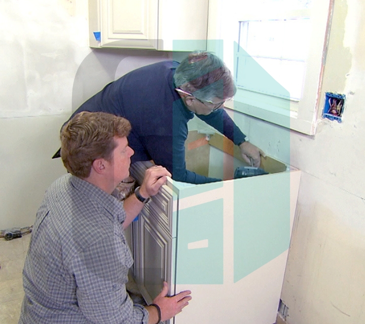 Two people installing base cabinets in a kitchen